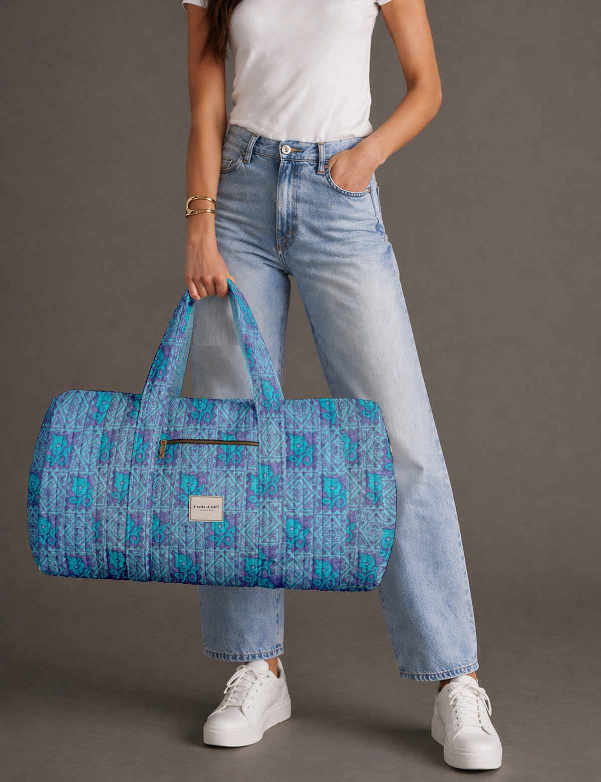 Quilted brown paisley barrel bag with double handles, front pocket, and gold zipper, shown in side angle view