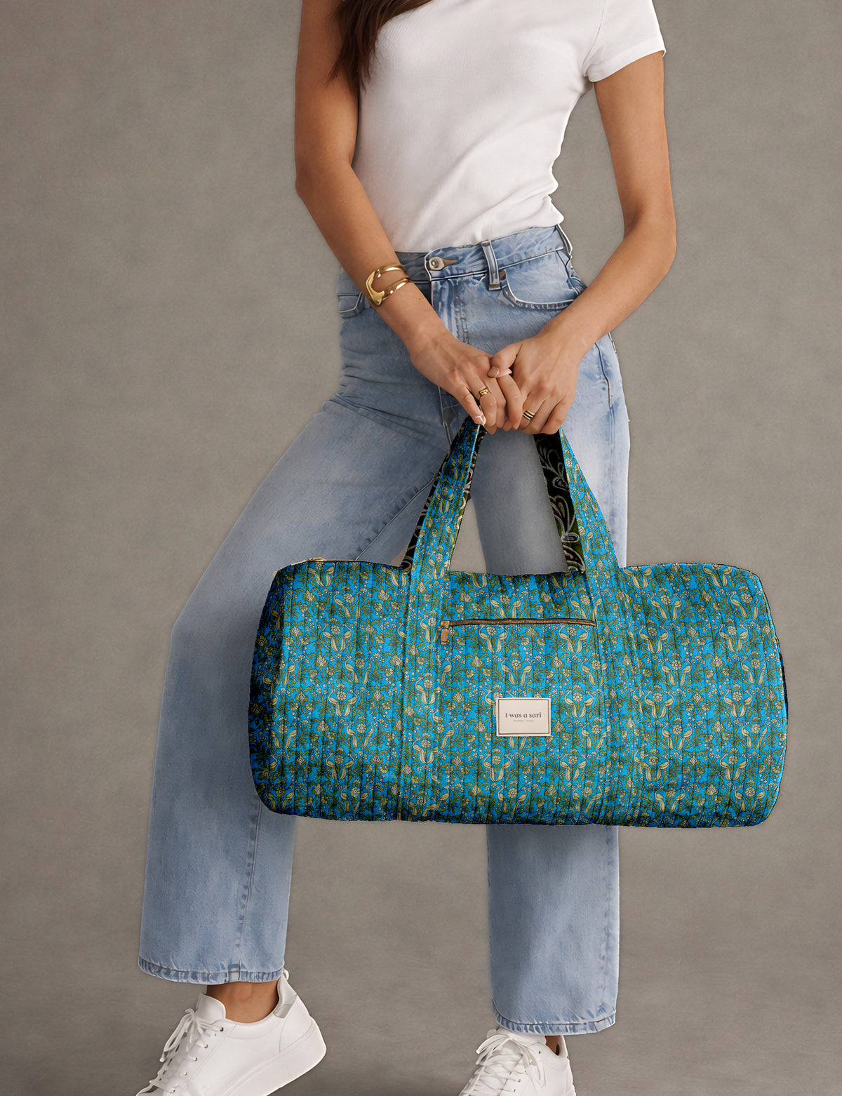 Brown paisley quilted bowling bag with front zipper pocket, held by person wearing white shirt and light blue jeans
