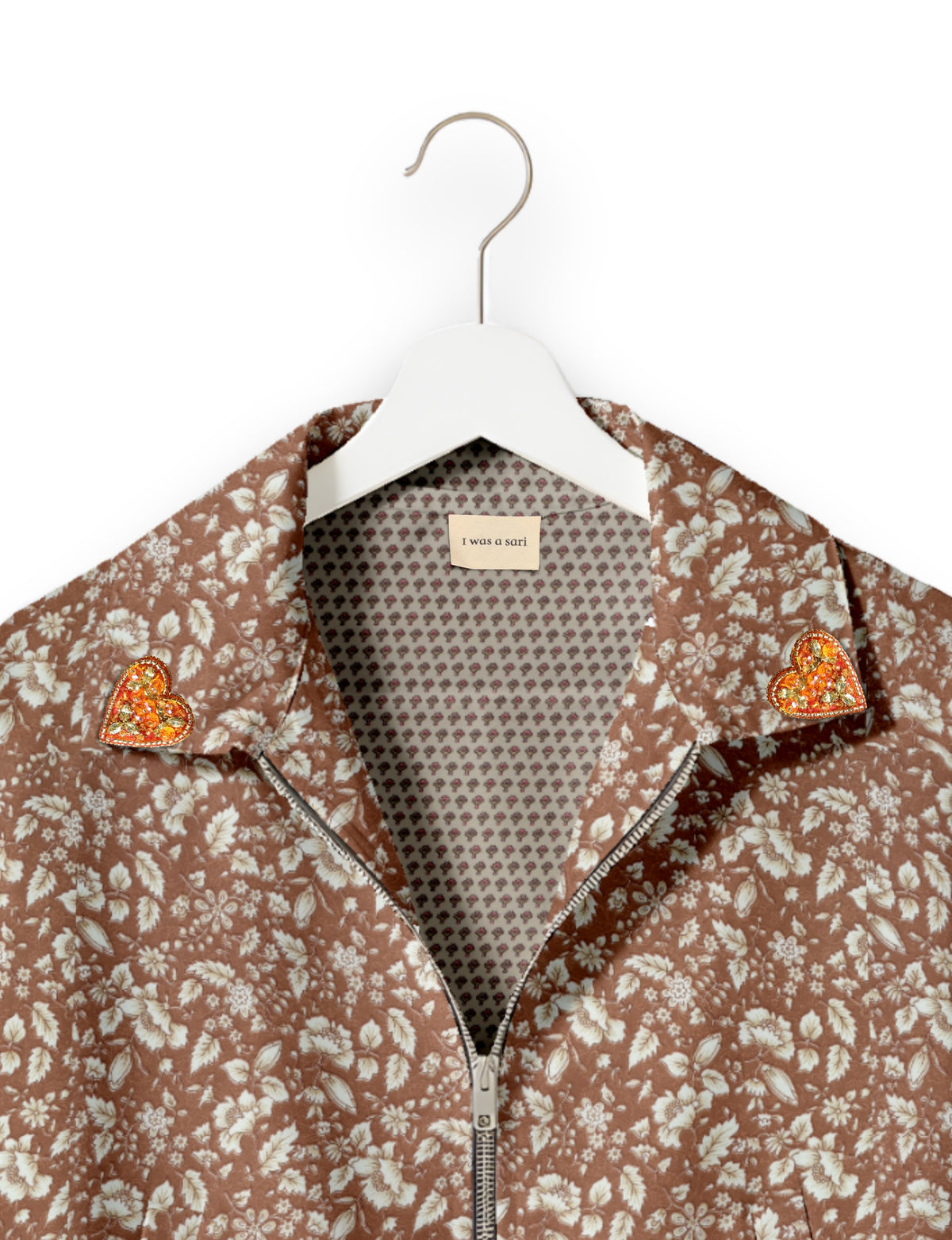 Brown floral bomber jacket with silver zipper and orange jeweled heart pins on collar, shown on white hanger