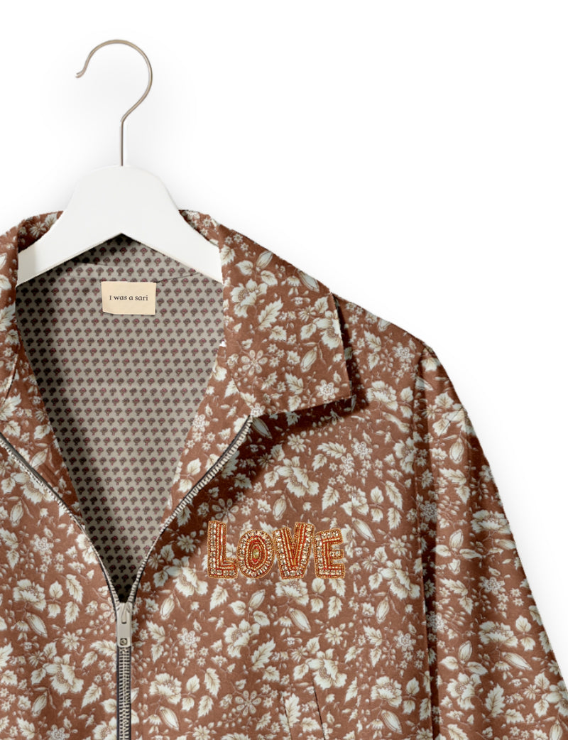 Brown floral bomber jacket with front zipper, beaded "LOVE" patch, and patterned inner lining on white hanger
