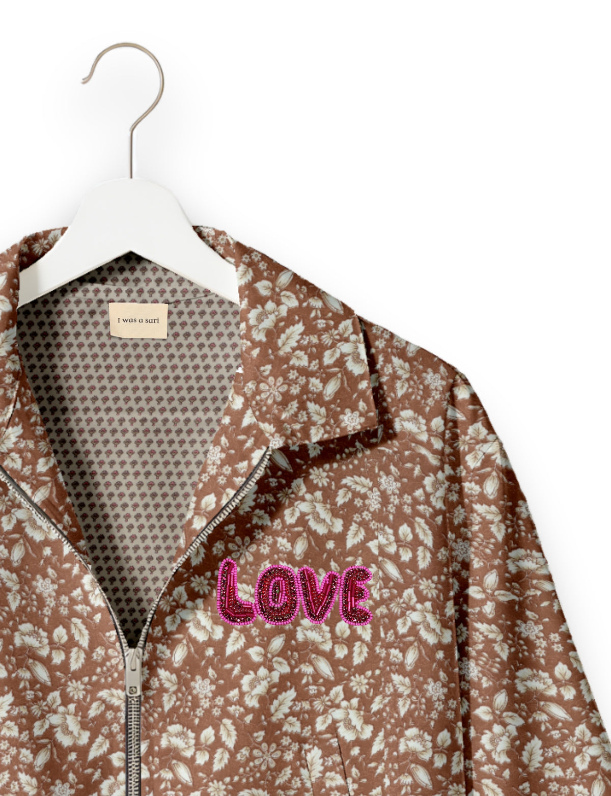 Brown floral bomber jacket with front zipper and pink beaded "LOVE" patch on chest, shown on white hanger