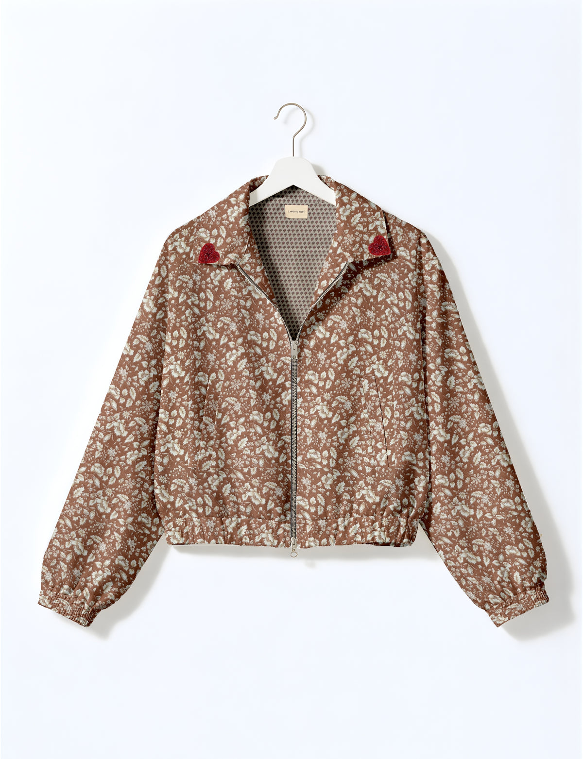 Brown floral bomber jacket with front zipper, elastic cuffs and hem, red heart patches on collar, hanging on white hanger