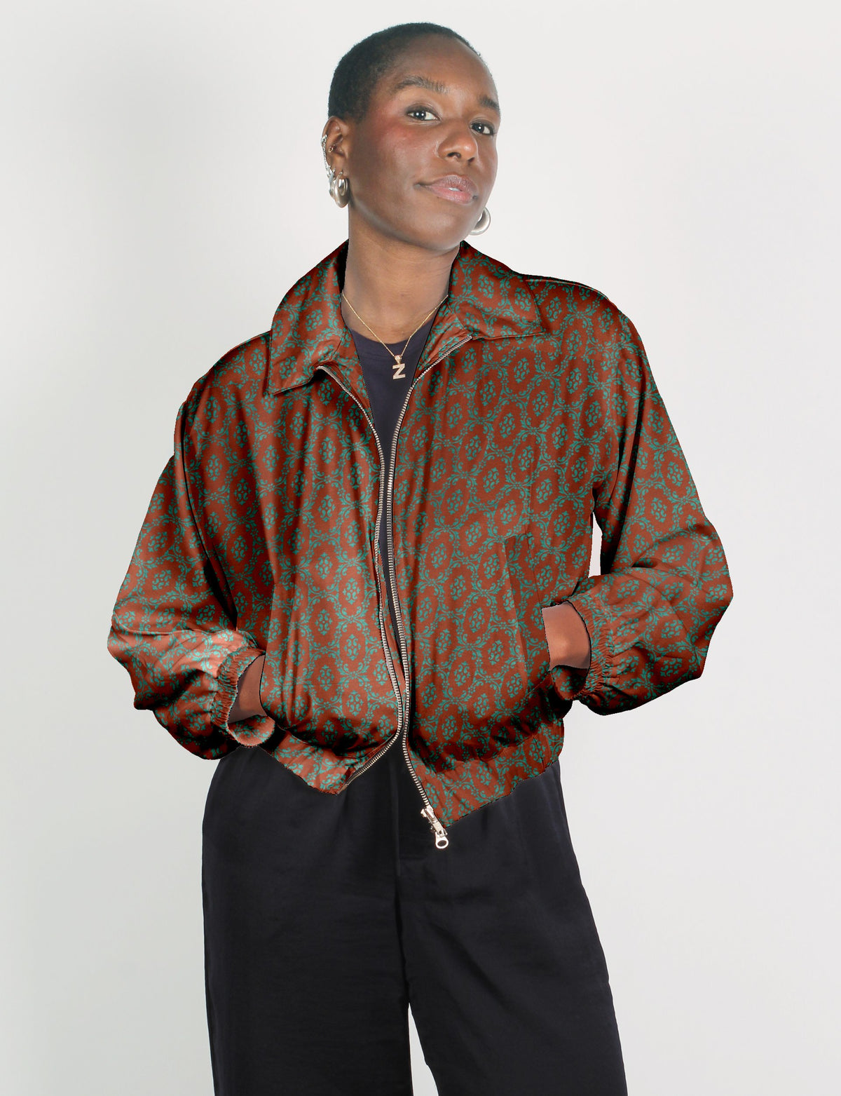 Woman wearing a brown bomber jacket with teal Indian ethnic pattern, front zipper, and elastic cuffs, paired with black