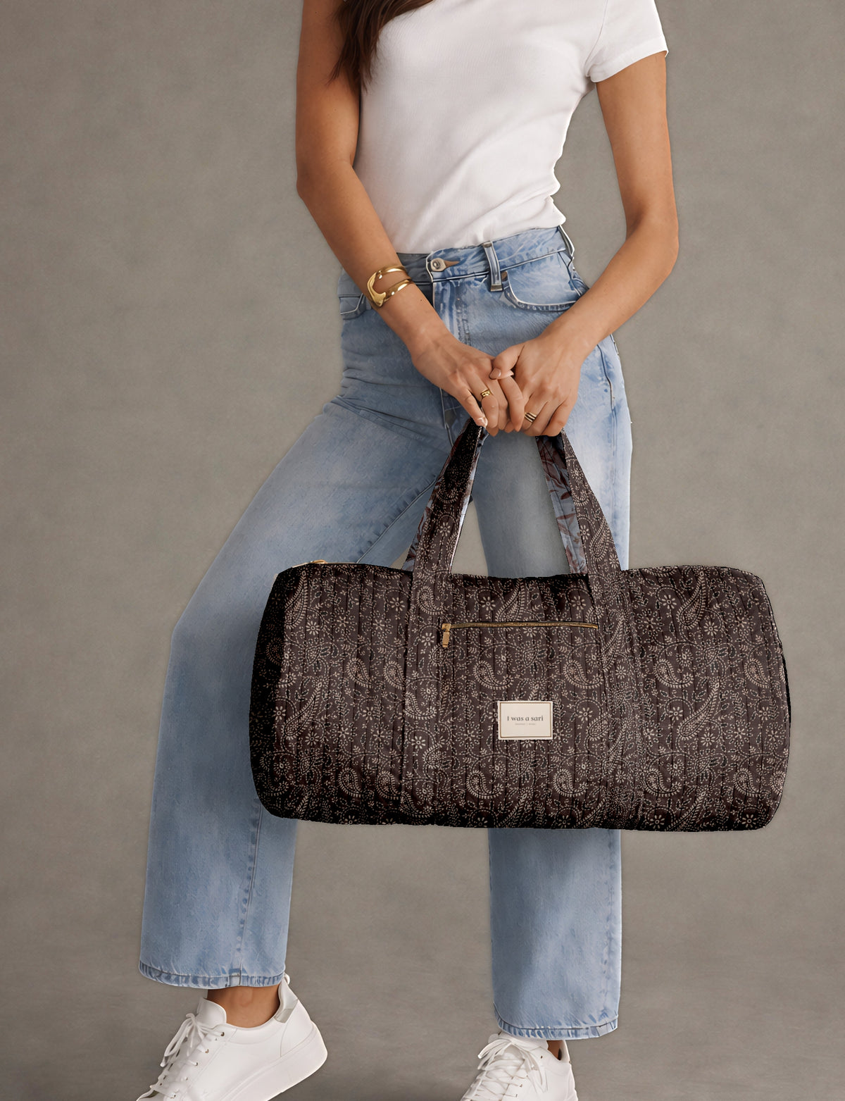 Brown paisley quilted bowling bag with front zipper pocket, held by person wearing white shirt and light blue jeans