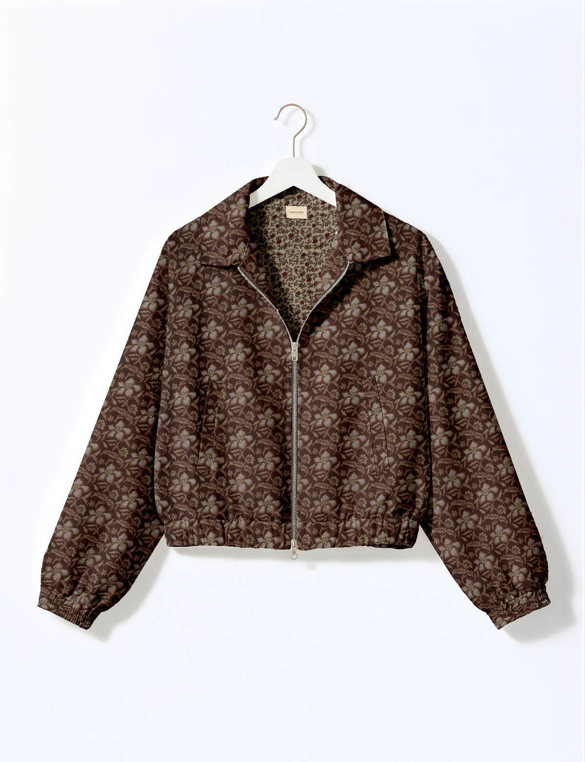 Brown bomber jacket with tropical floral pattern, front zipper, elastic cuffs and hem, hanging on white hanger front view