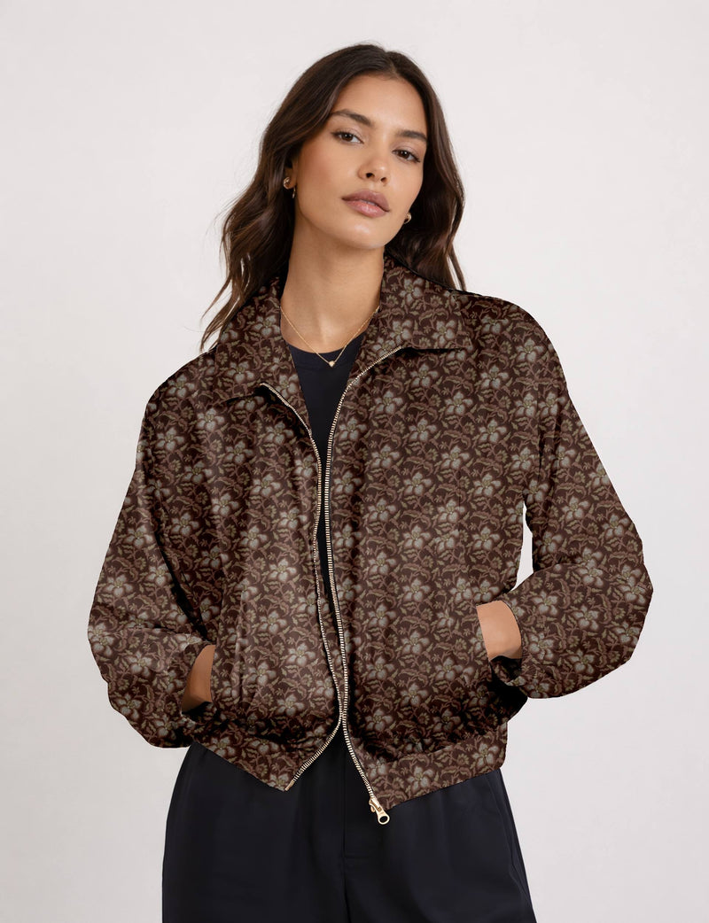 Woman wearing brown bomber jacket with tropical floral pattern, front zipper, and side pockets, paired with black pants