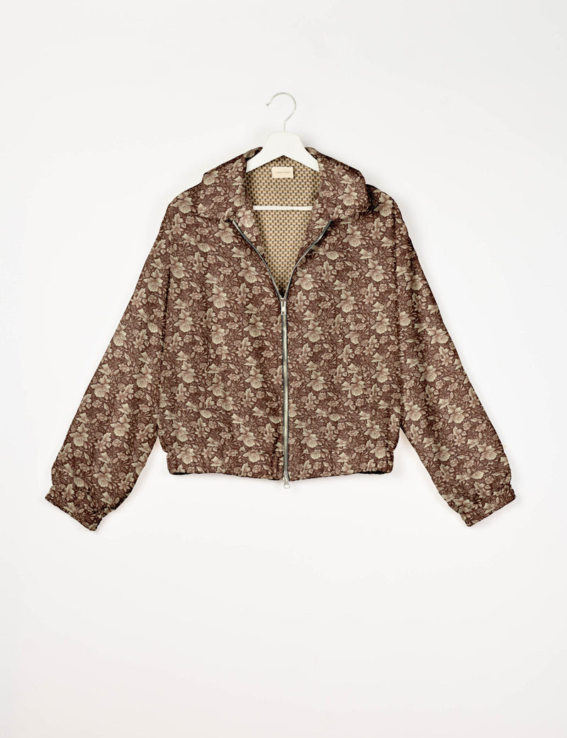 Brown bomber jacket with tropical floral pattern, front zipper, elastic cuffs, and contrasting small geometric print lining