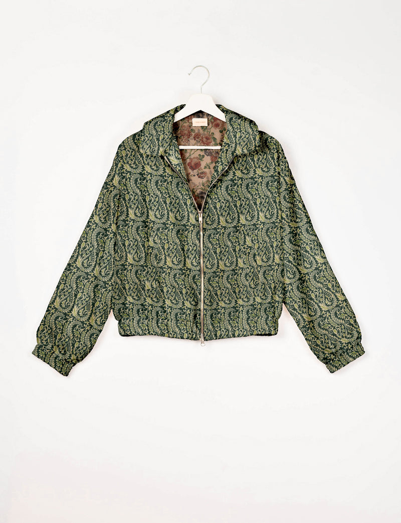 Green bomber jacket with cream leaf pattern, front zipper, elastic cuffs, and floral inner lining, hanging on white hanger