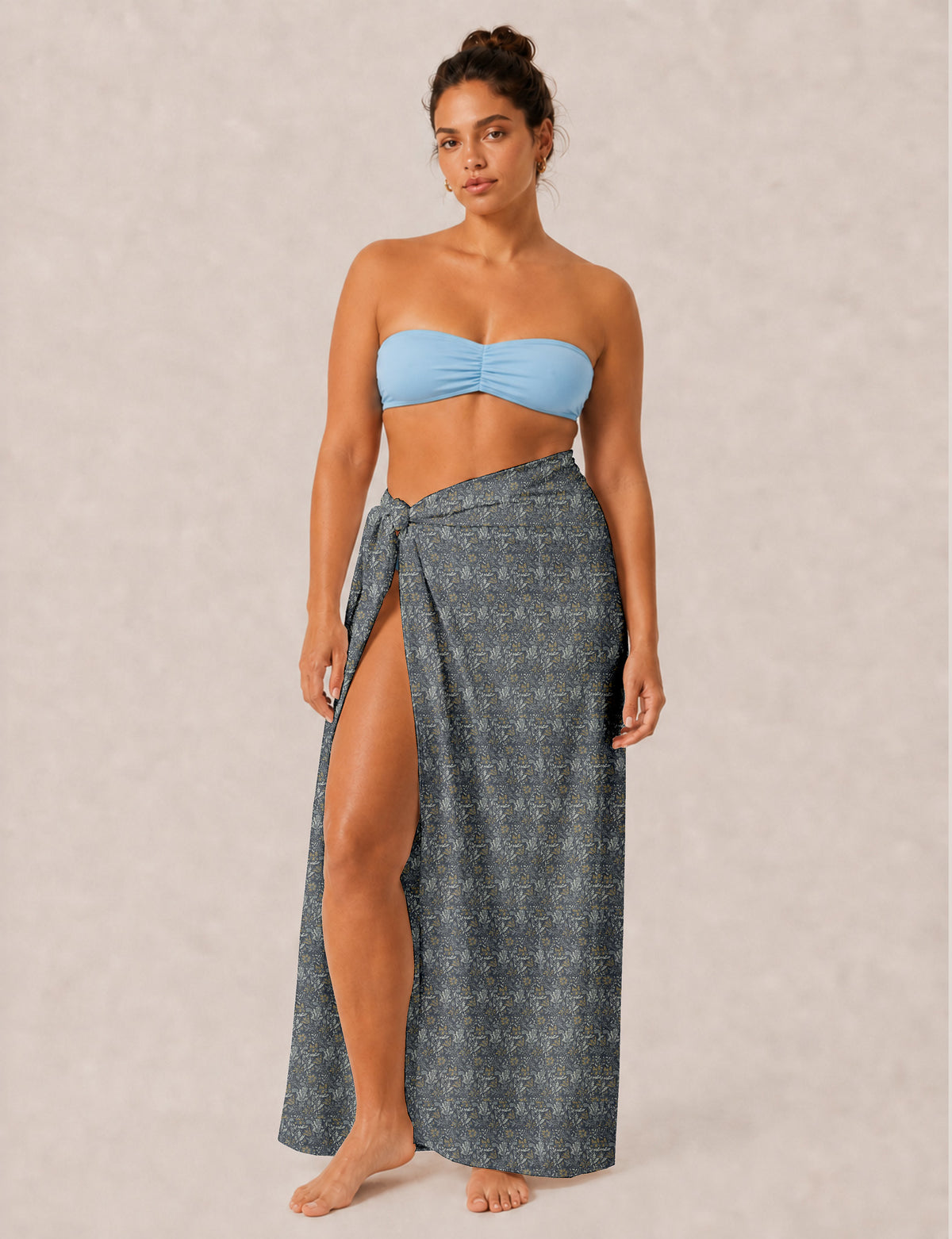 Woman wearing a grey tropical print pareo tied at the waist with a high slit, paired with a light blue bandeau top