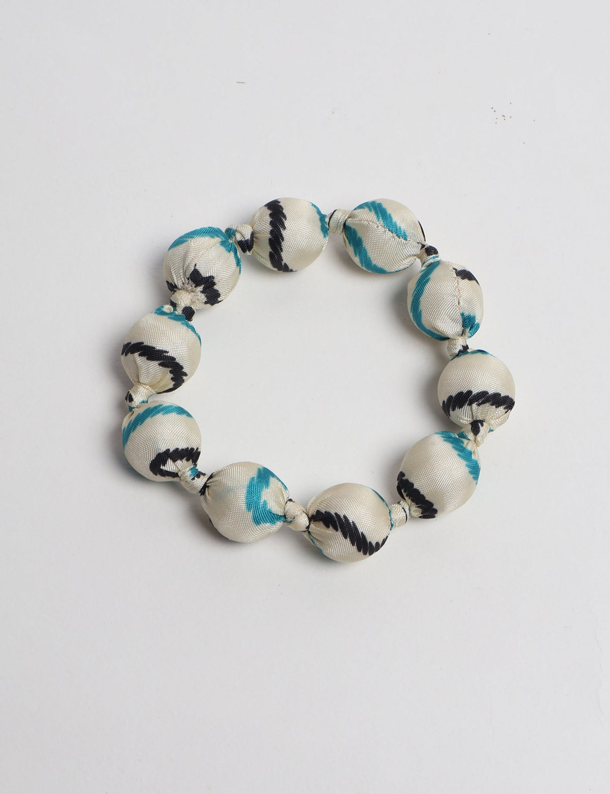 White fabric beaded bracelet with black and teal tropical pattern, knotted between each bead, flat lay on white background