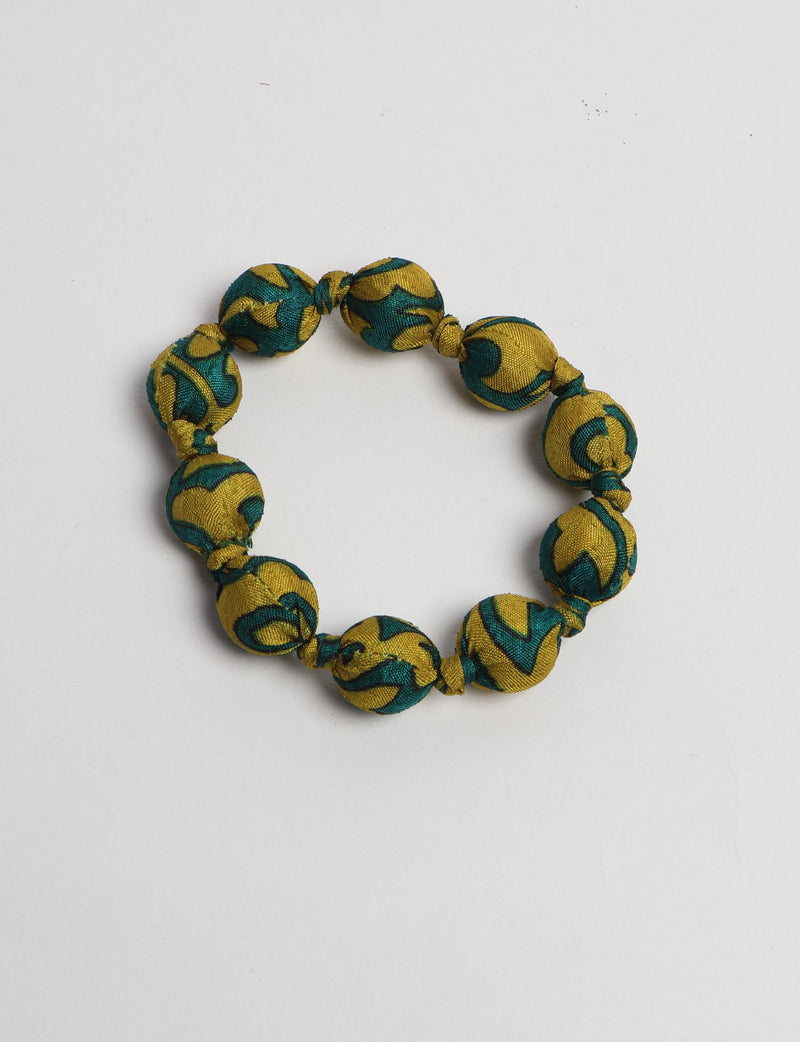Yellow and green patterned fabric beaded bracelet with knotted details, shown flat on a white background