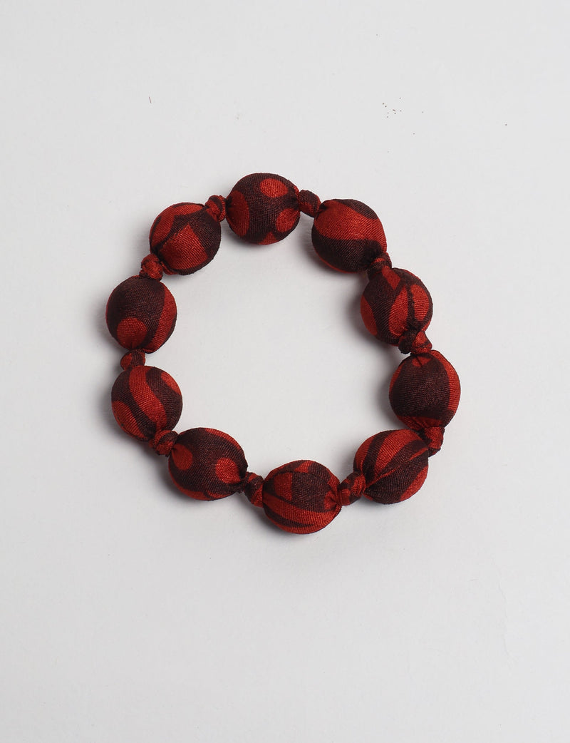 Red and dark brown fabric beaded bracelet with knotted details, flat lay on white background