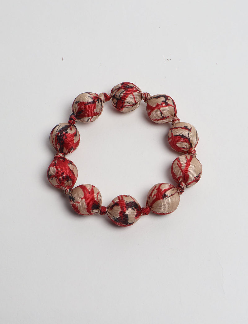 Knotted bracelet with round fabric beads in beige, red, and black abstract pattern, flat lay on white background
