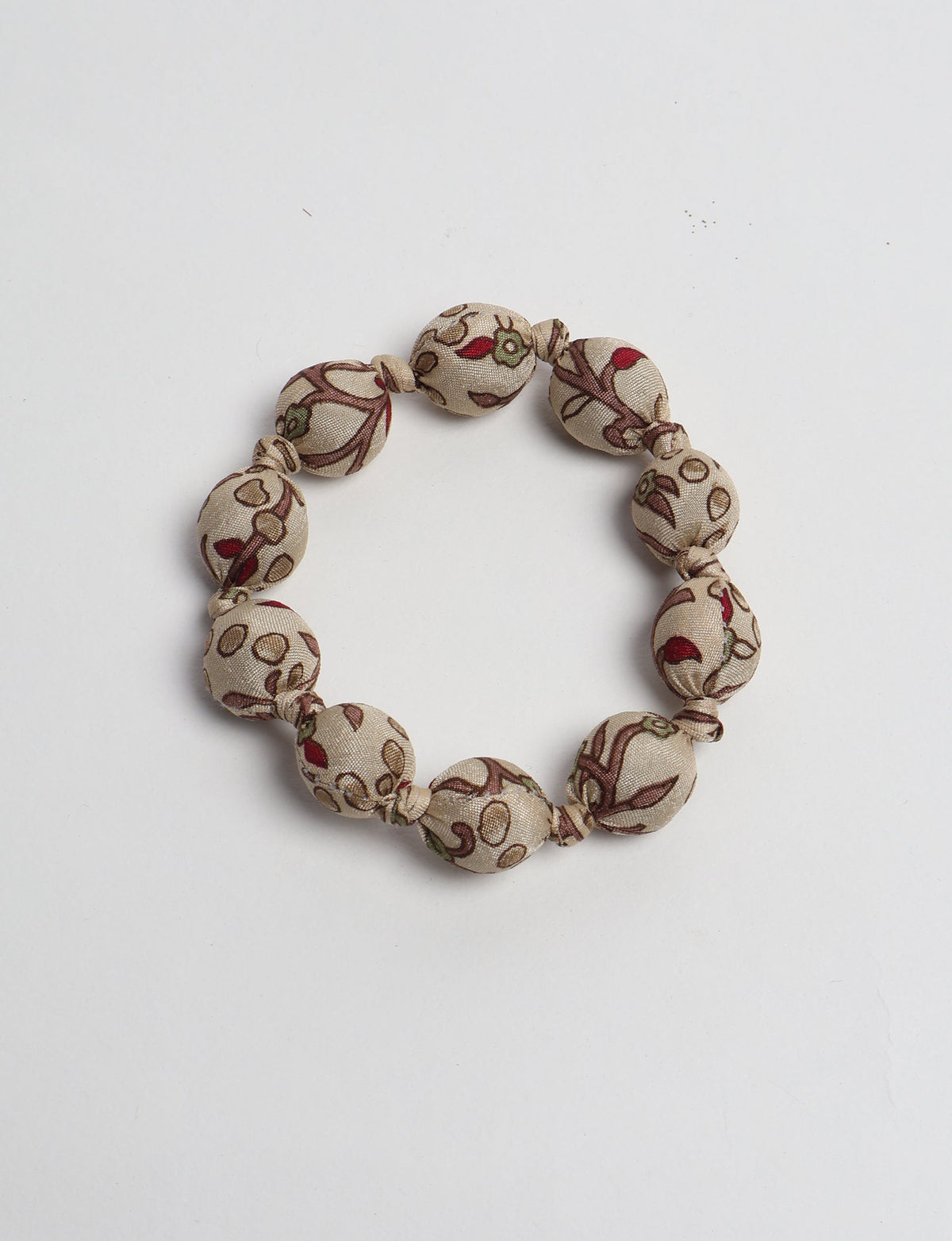 Beige fabric beaded bracelet with knotted design and tropical floral pattern in red, green, and brown, flat lay view