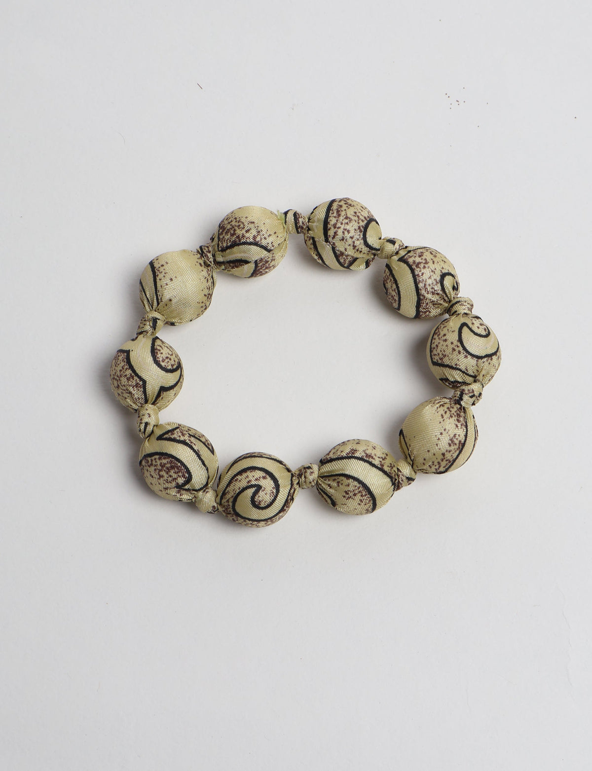 Beaded knotted bracelet with beige fabric-covered round beads featuring brown and black tropical swirl patterns, flat lay