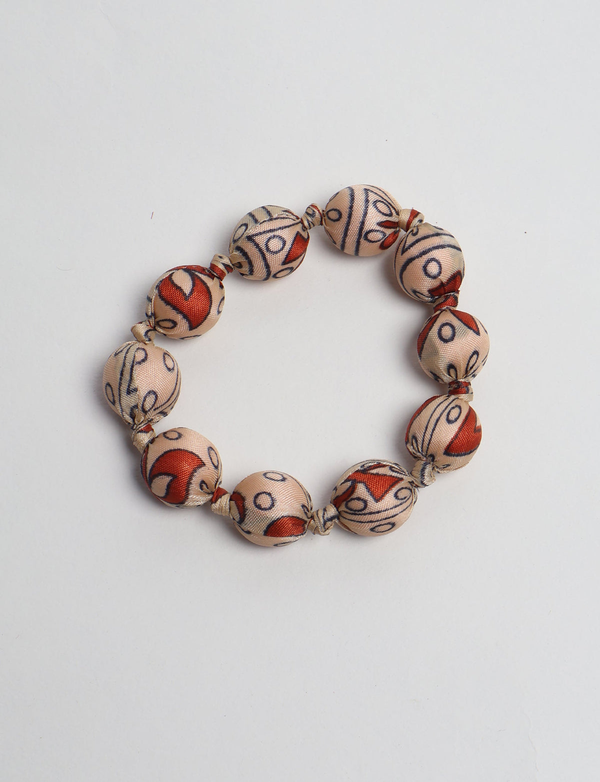 Beaded knotted bracelet with beige fabric-covered round beads featuring red and black tropical patterns, flat lay view