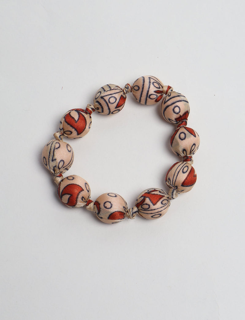 Beaded knotted bracelet with beige fabric-covered round beads featuring red and black tropical patterns, flat lay view