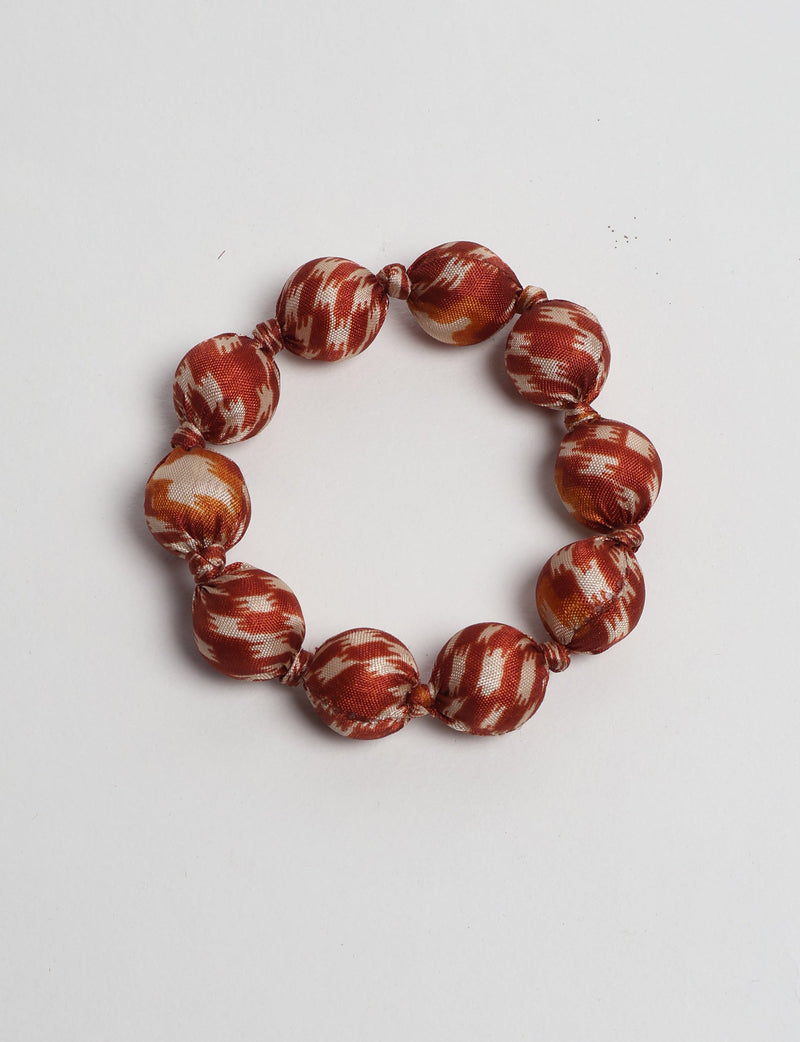 Knotted bracelet with large fabric-covered beads in orange and cream tropical pattern, shown flat on white background