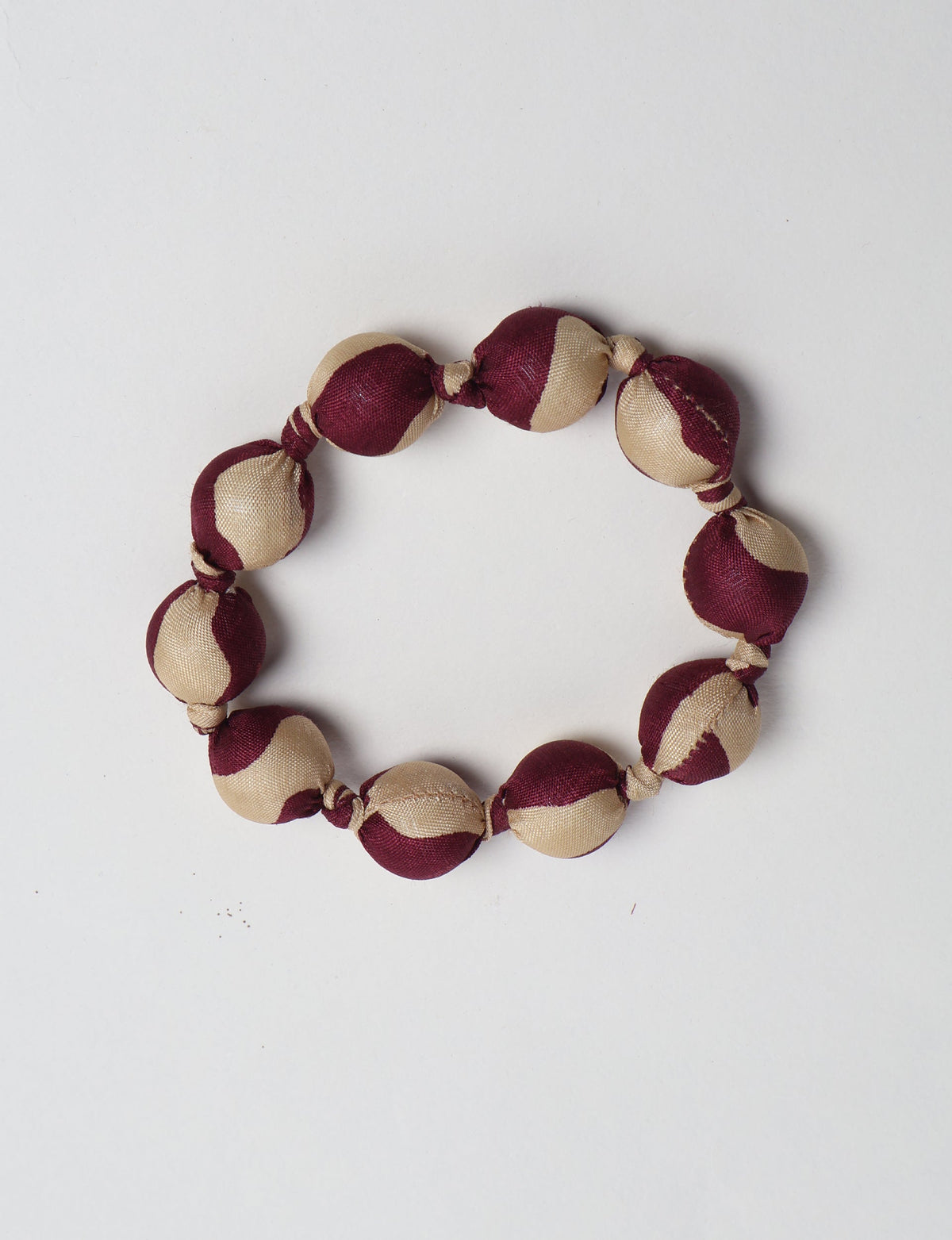Beaded knotted bracelet with alternating beige and dark red fabric-covered round beads, flat lay on white background