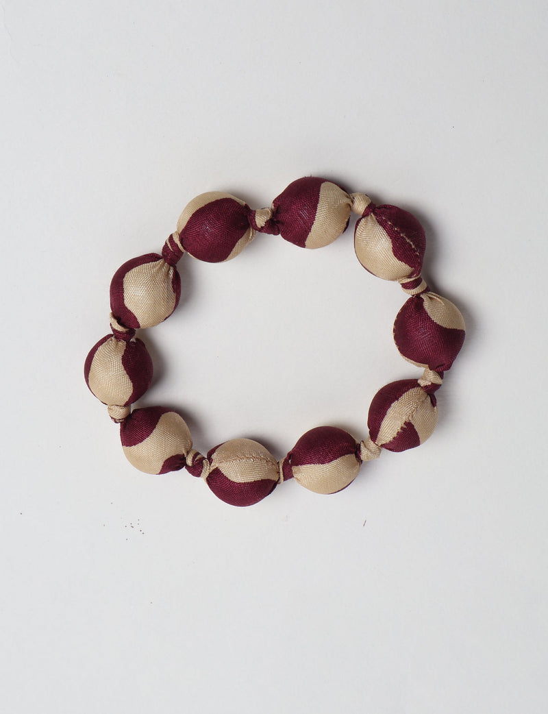 Beaded knotted bracelet with alternating beige and dark red fabric-covered round beads, flat lay on white background