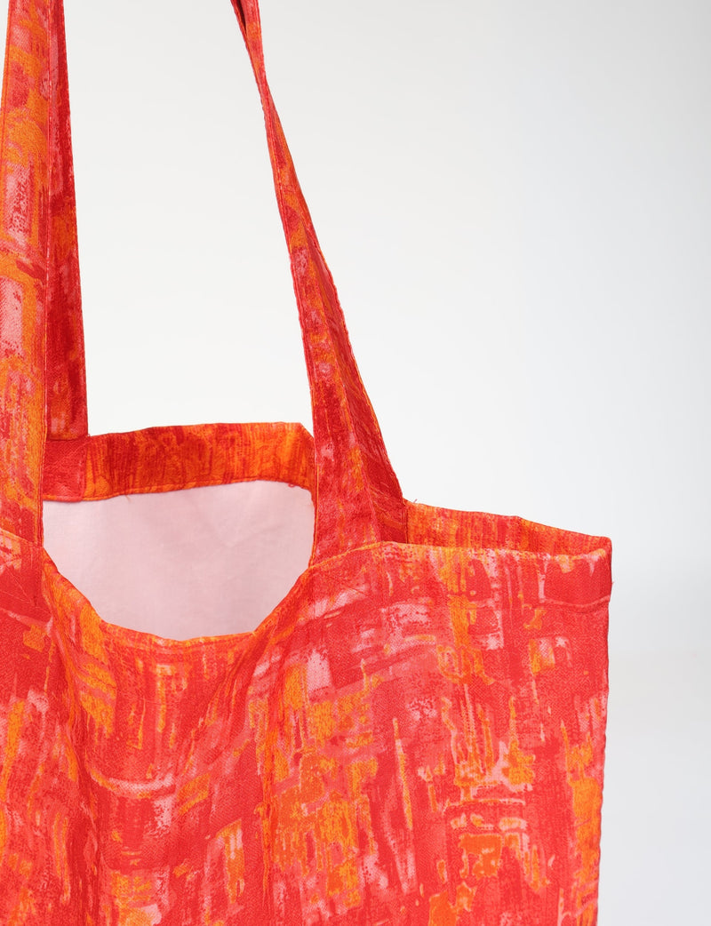 Orange abstract patterned fabric shopper bag with long handles shown in close-up front view hanging