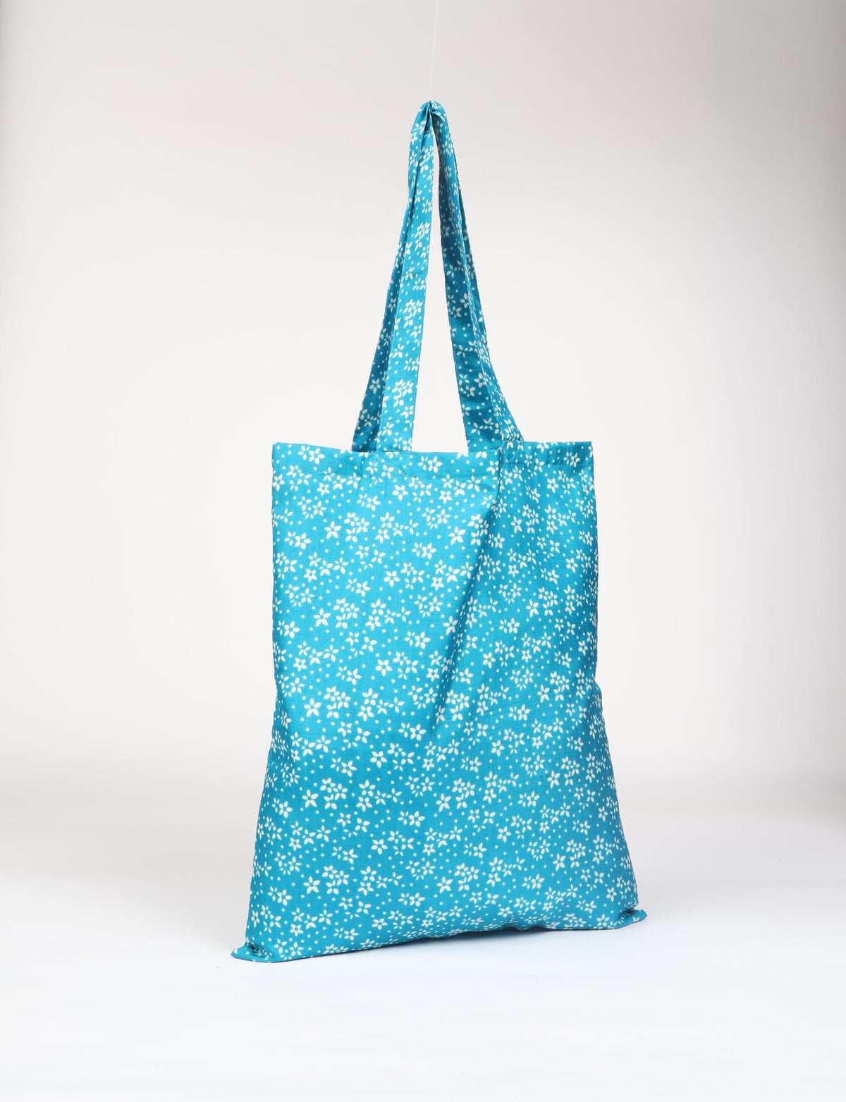Blue fabric shopper bag with white small floral print, long handles, shown hanging against a plain background