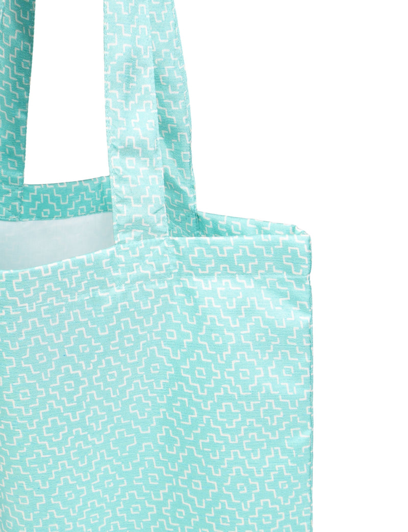 Blue shopper bag with white geometric pattern, close-up of top corner and handle, fabric texture visible