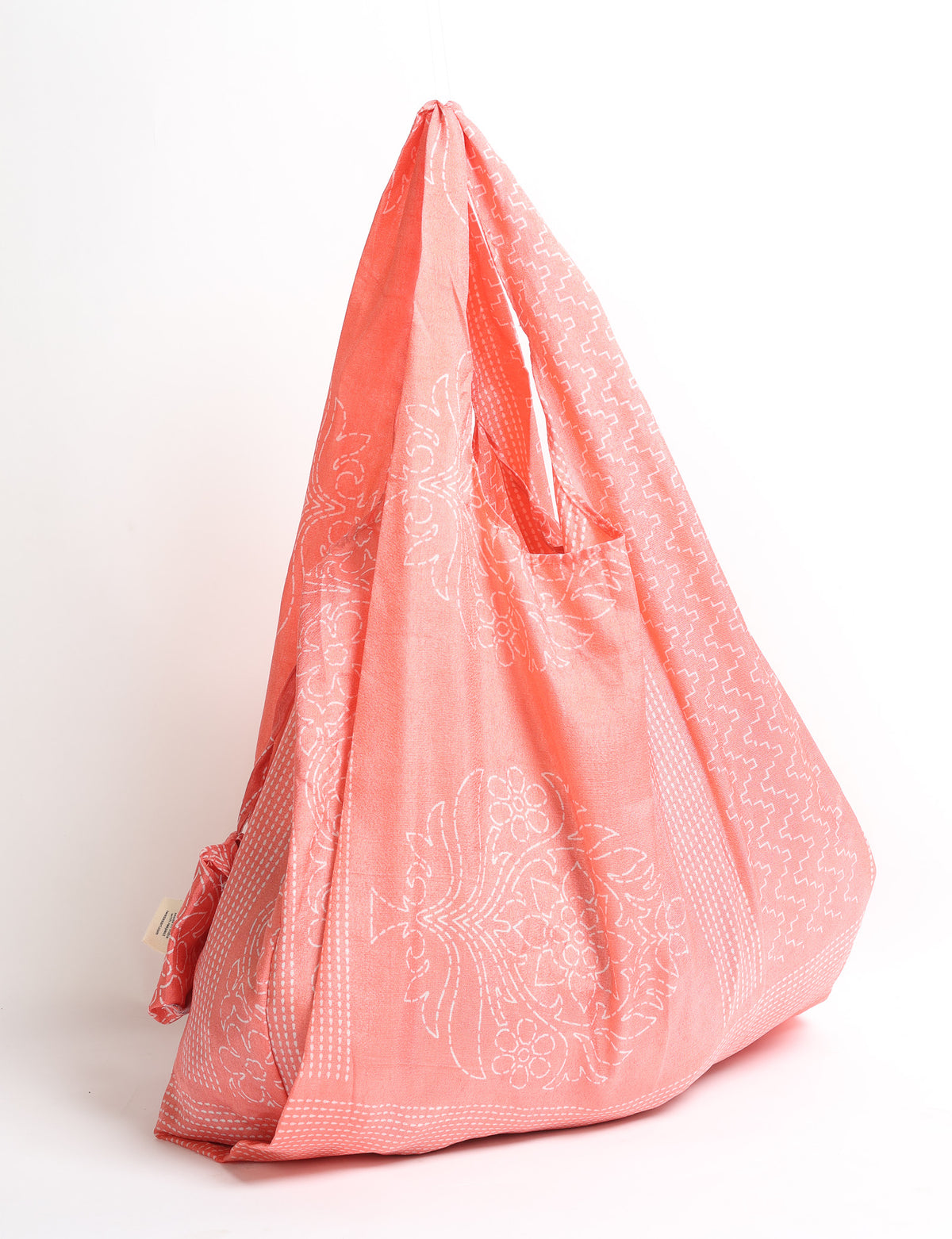 Pink reusable bag with white floral and geometric patterns, hanging by its handles against a white background