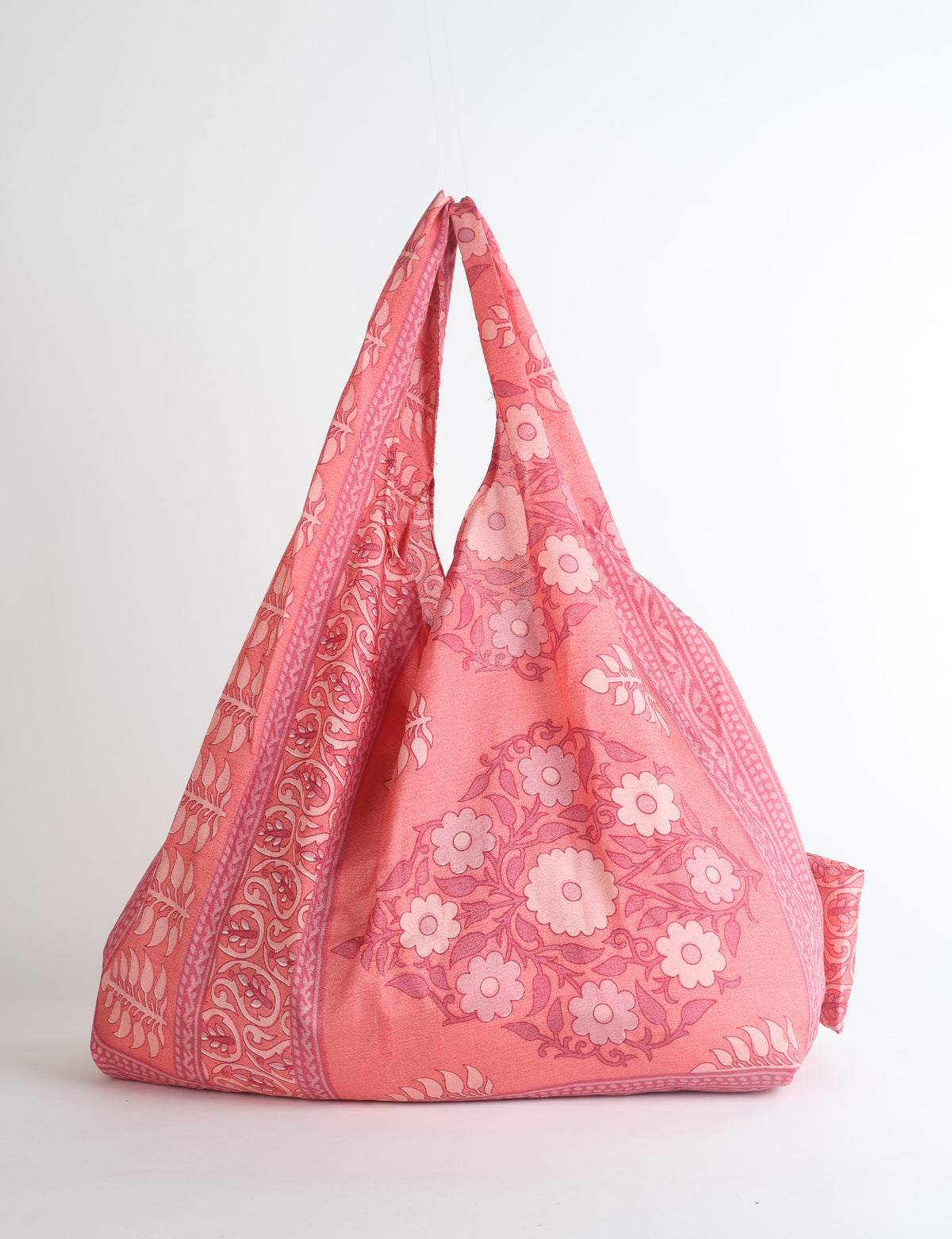 Pink reusable bag with paisley and floral patterns, shown hanging with handles together against a white background