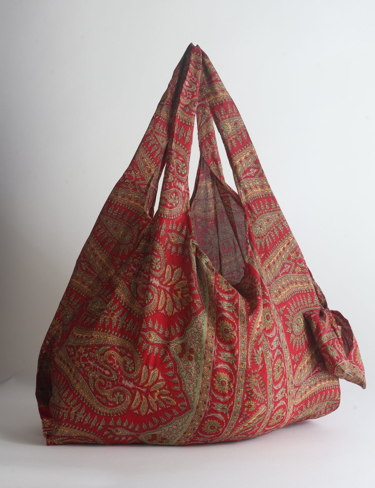 Blue reusable bag with tropical floral pattern in pink, yellow, and green, shown hanging with handles visible
