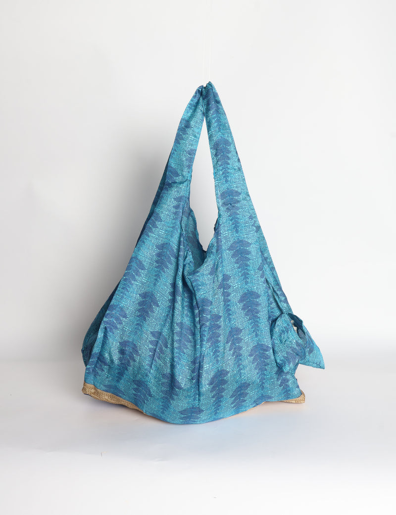 Blue reusable bag with tropical floral pattern in pink, yellow, and green, shown hanging with handles visible