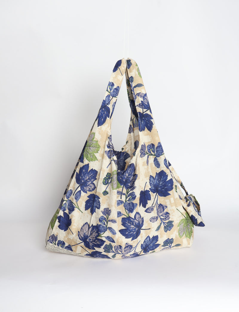 Blue reusable bag with tropical floral pattern in pink, yellow, and green, shown hanging with handles visible