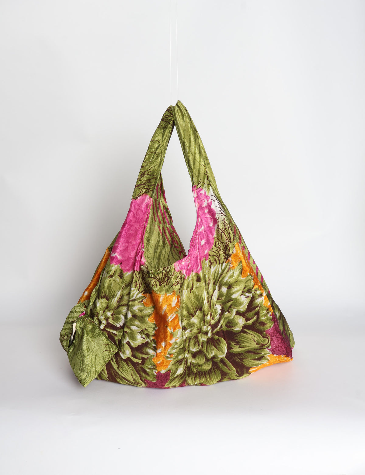 Blue reusable bag with tropical floral pattern in pink, yellow, and green, shown hanging with handles visible