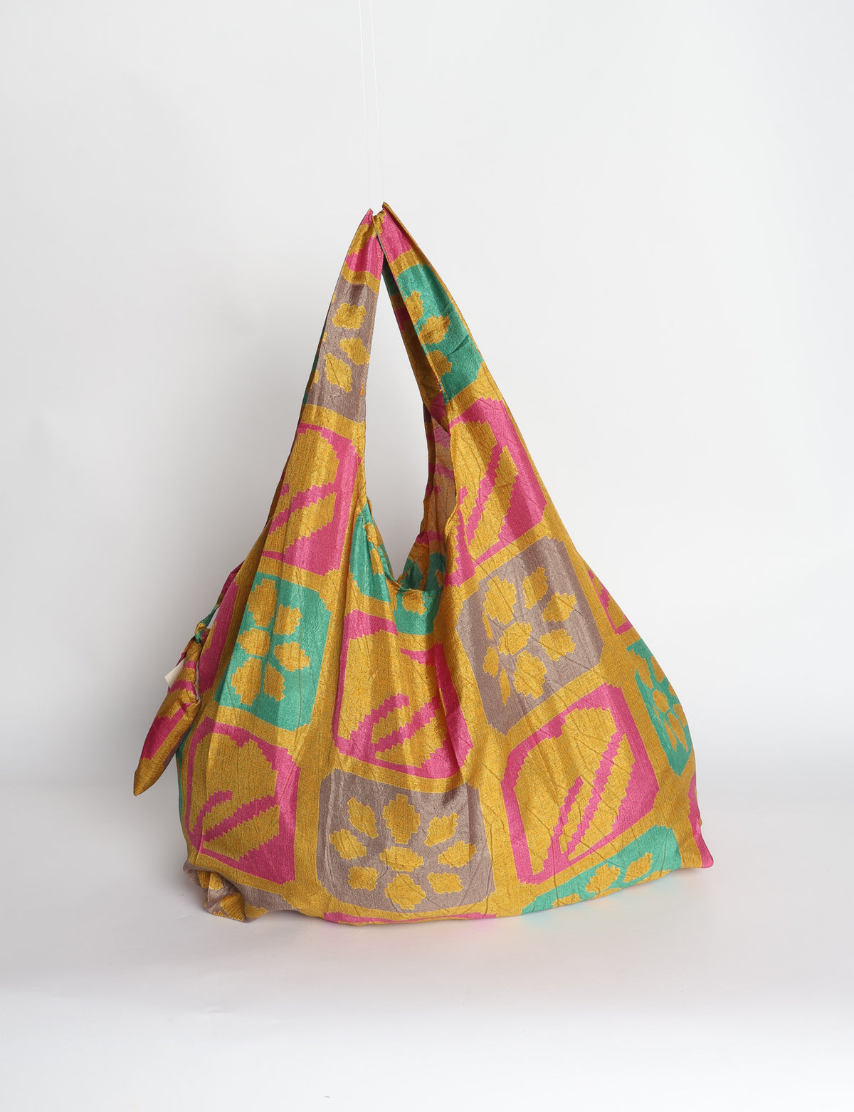 Blue reusable bag with tropical floral pattern in pink, yellow, and green, shown hanging with handles visible