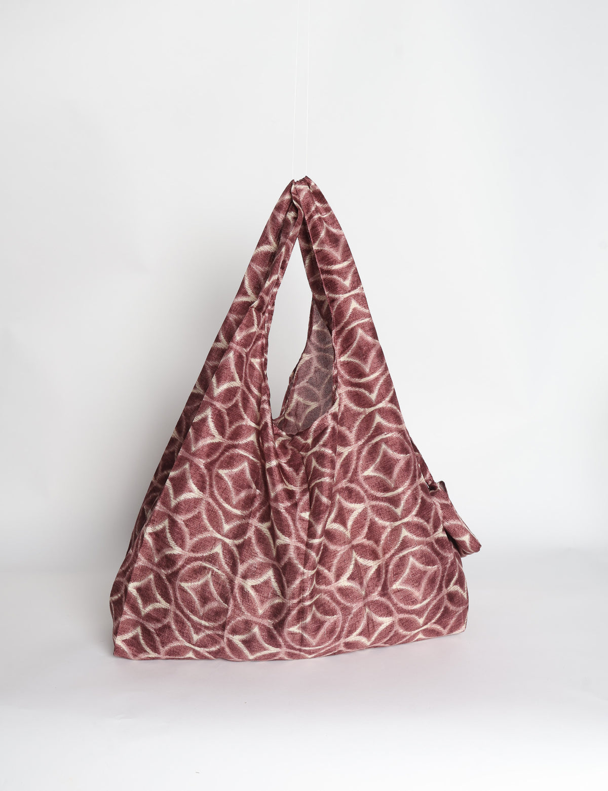 Blue reusable bag with tropical floral pattern in pink, yellow, and green, shown hanging with handles visible