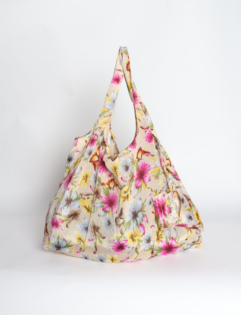 Blue reusable bag with tropical floral pattern in pink, yellow, and green, shown hanging with handles visible
