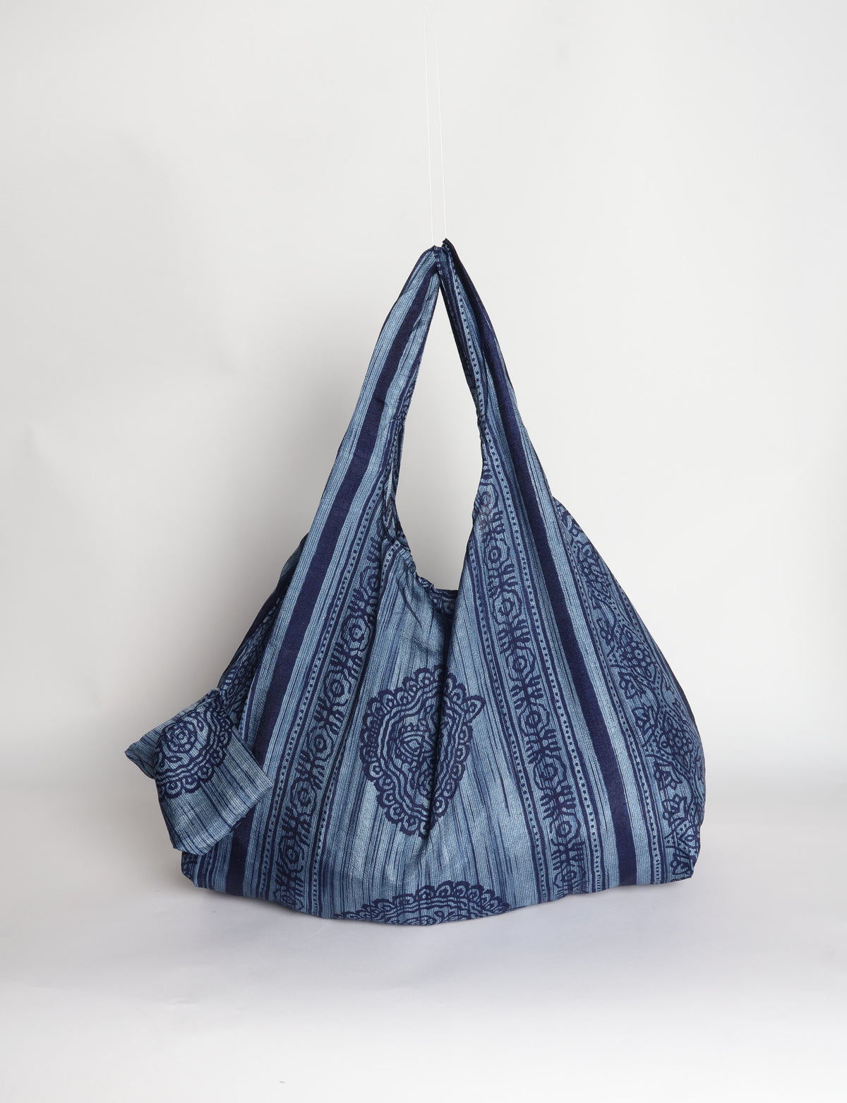 Blue reusable bag with tropical floral pattern in pink, yellow, and green, shown hanging with handles visible