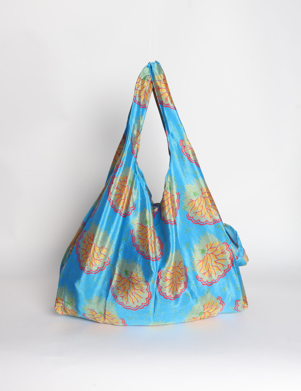 Blue reusable bag with tropical floral pattern in pink, yellow, and green, shown hanging with handles visible