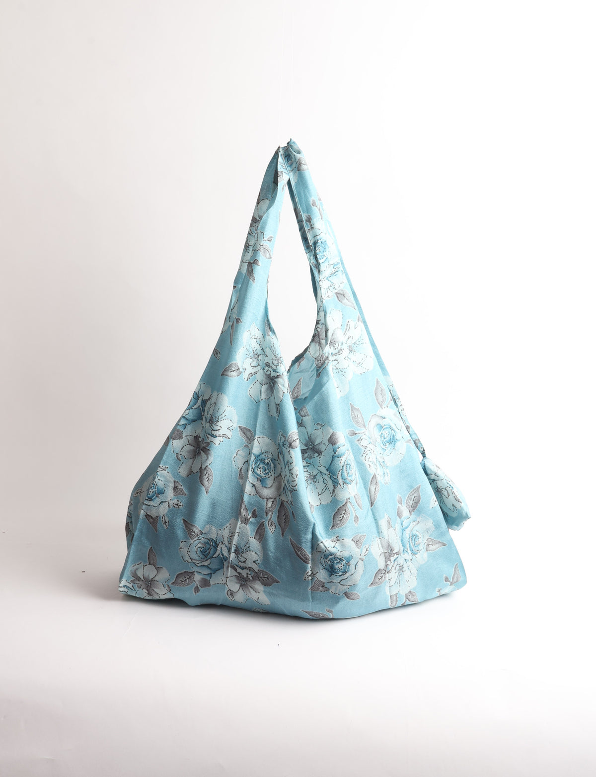 Blue reusable bag with tropical floral pattern in pink, yellow, and green, shown hanging with handles visible