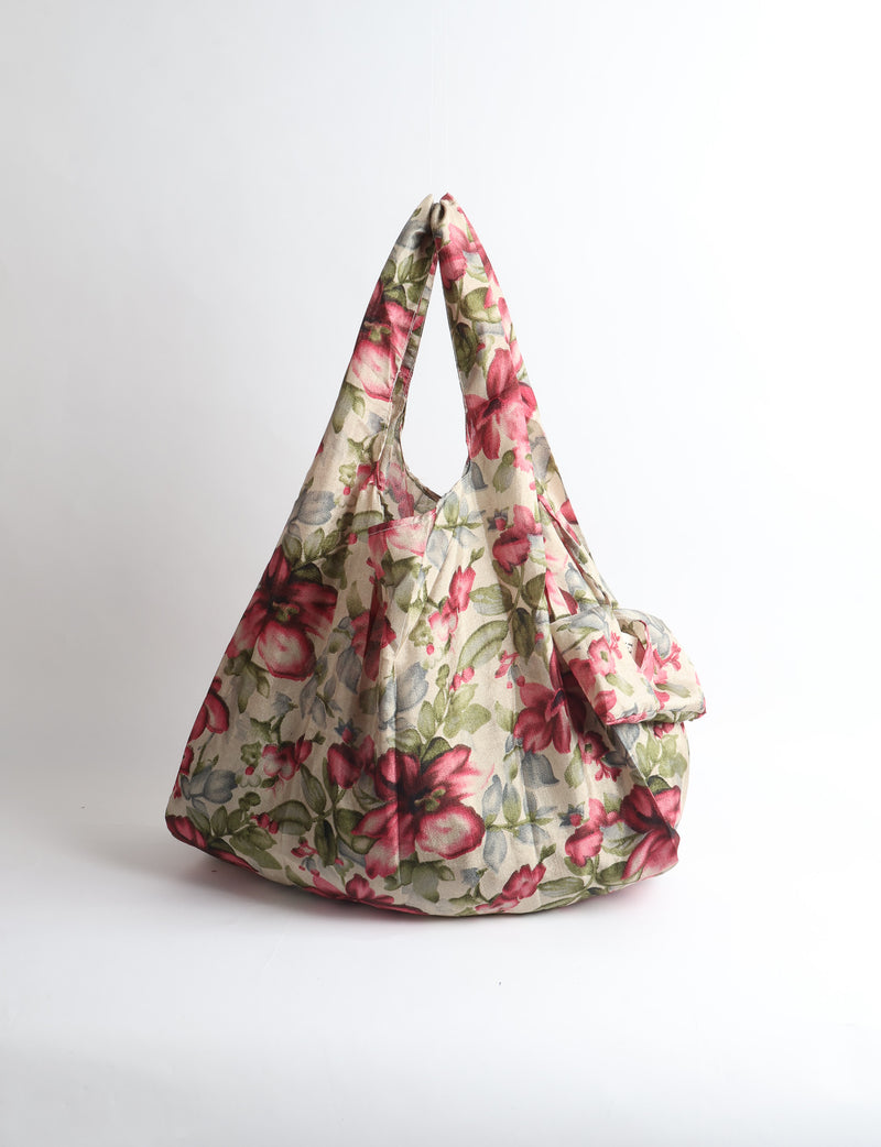 Blue reusable bag with tropical floral pattern in pink, yellow, and green, shown hanging with handles visible