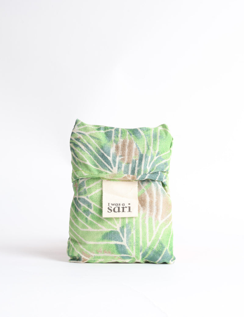Blue reusable bag with tropical floral pattern in pink, yellow, and green, shown hanging with handles visible
