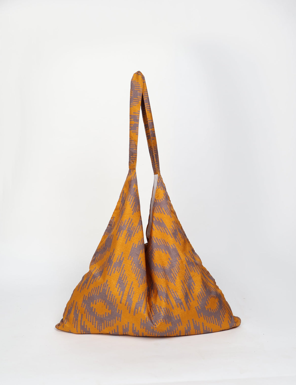Yellow and brown ikat patterned trapeze bag with long handles, shown hanging against a white background