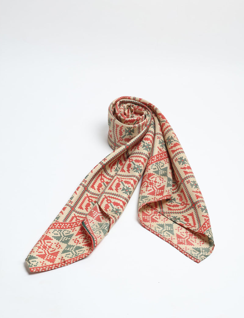 Beige foulard with red and green Indian ethnic geometric patterns, rolled and laid flat on white background