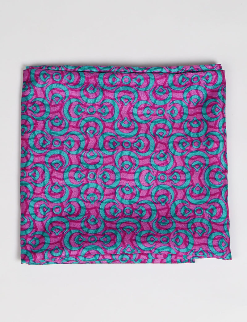 Folded loop scarf with pink background and teal abstract circular pattern, flat lay on white surface