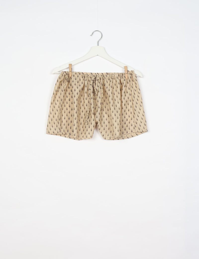 Beige shorts with micro dark brown pattern, elastic waistband with drawstring, hanging on white hanger, front view