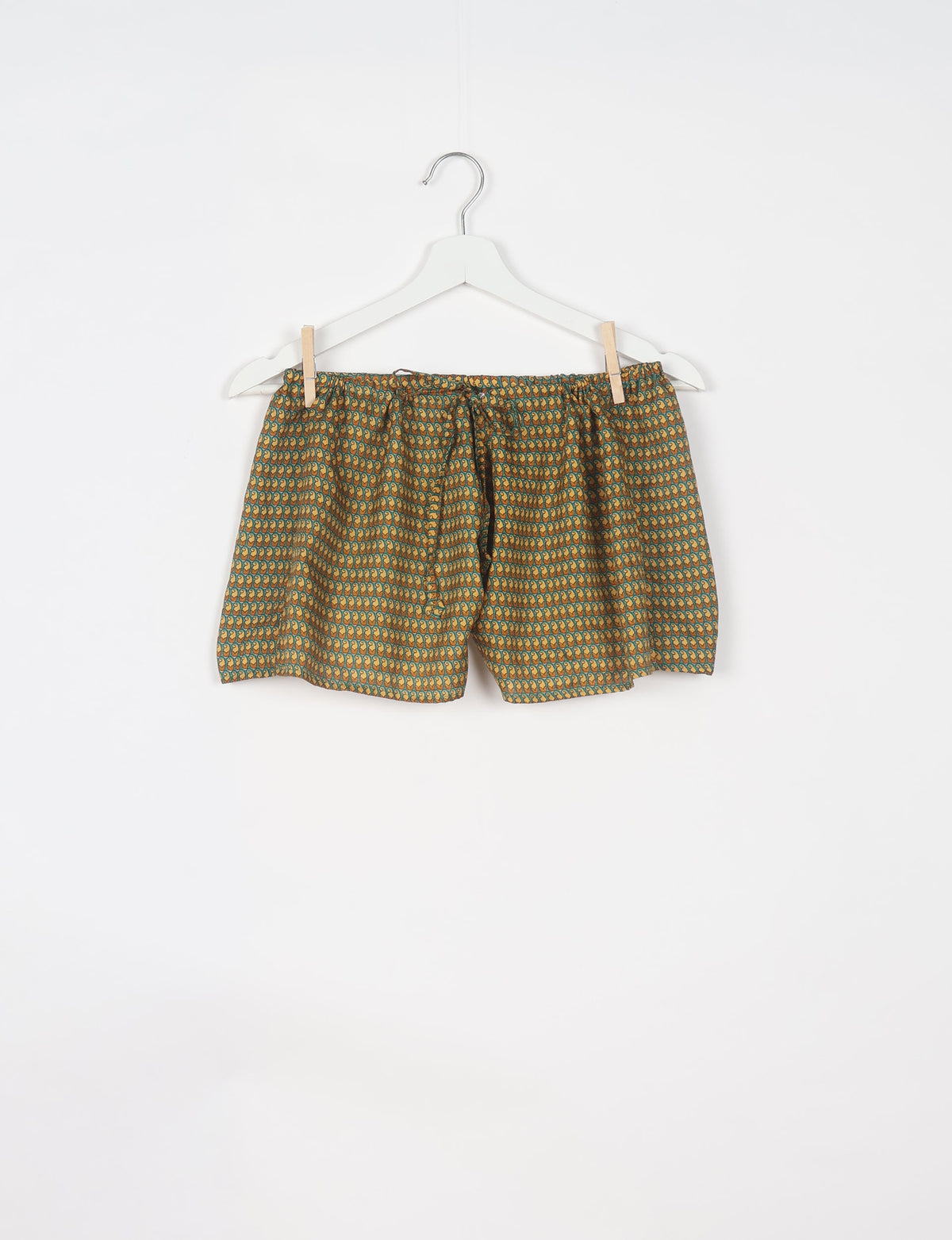 Green shorts with micro paisley design in yellow and orange, elastic waistband with drawstring, hanging on white hanger