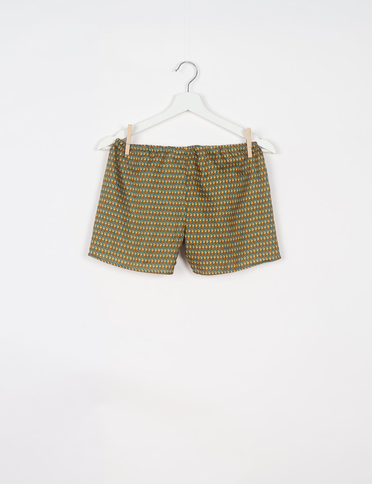 Green shorts with micro paisley pattern in yellow and blue, hanging on white hanger against white background