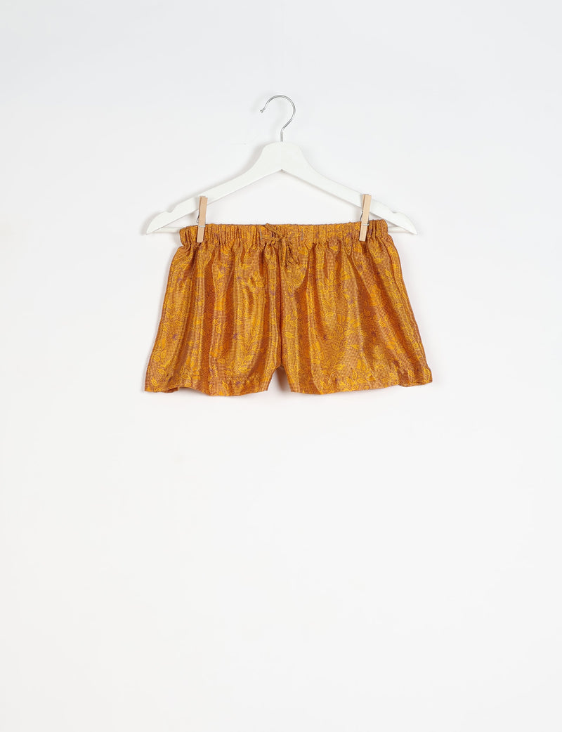 Yellow tropical print shorts with elastic waistband and drawstring, hanging on white hanger against white background