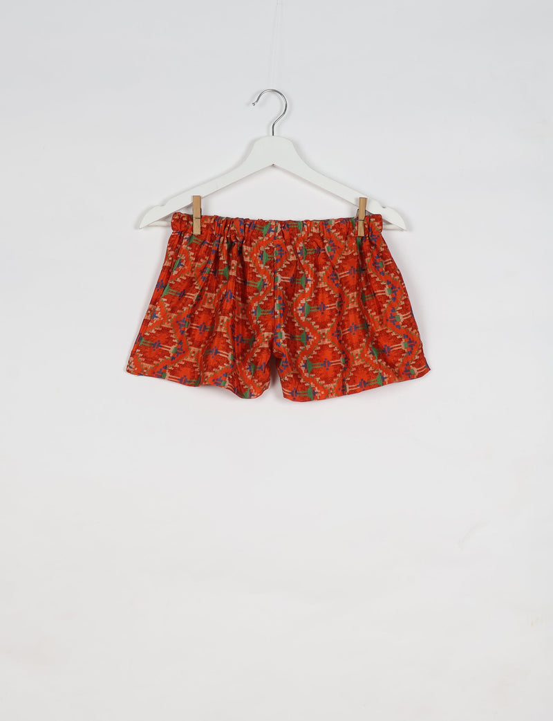 Orange ethnic patterned shorts with elastic waistband hanging on white hanger against white background