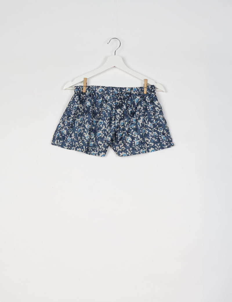 Blue tropical print shorts with elastic waistband hanging on white hanger against white background